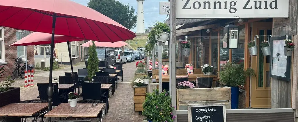 Buitenkant van restaurant Zonnig Zuid van het terras met tafels en stoelen en rode parasols