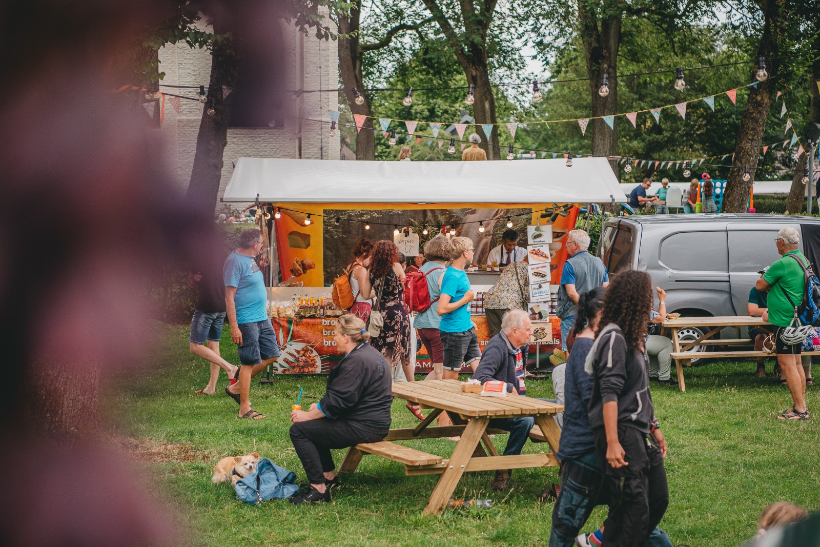 Sfeerbeeld van een marktkraam met gezellige lampjes, vlaggetjes en verschillende personen die langs lopen